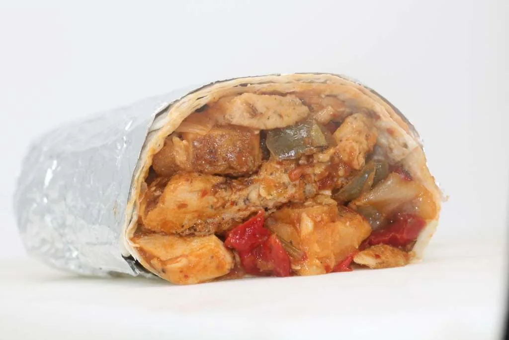 A burrito cut in half and wrapped in foil, filled with chicken, potato and bell pepper.