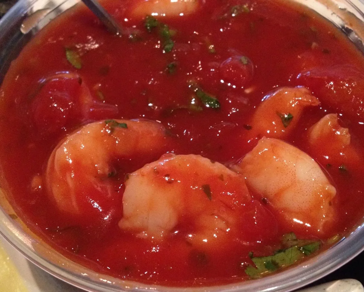 Whole shrimp in red salsa in a metal pan, with a spoon.
