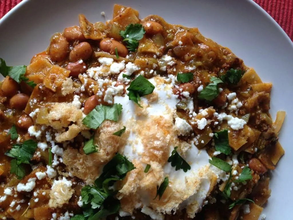 Chilaquiles with beans, crema, queso fresco and cilantro in a deep bowl.