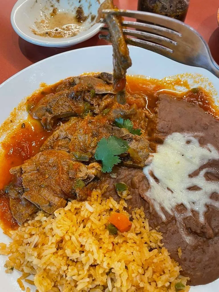 Ribs in salsa with rice and refried beans with cheese, on a white plate.
