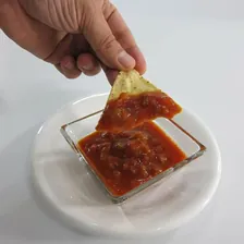 A hand lifting a tortilla chip out of a bowl of salsa