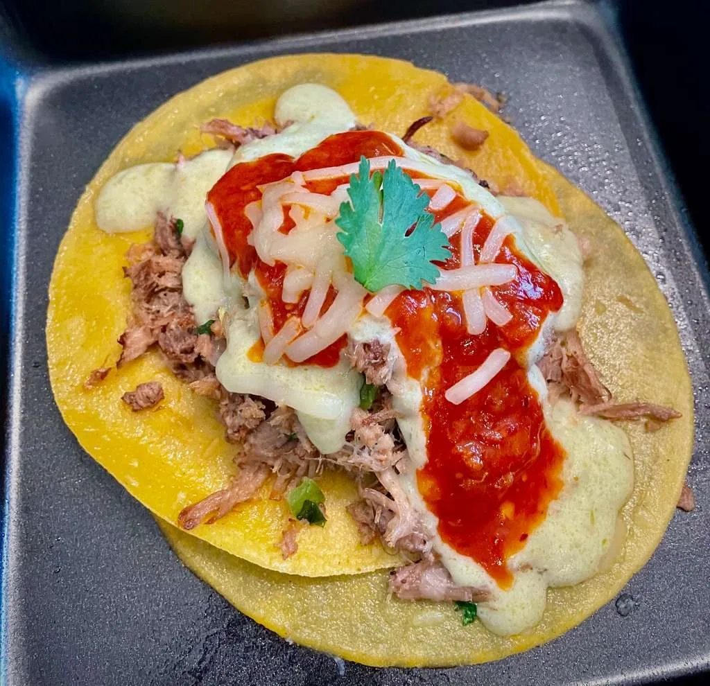 An open tortilla with shredded beef, melted cheese, red salsa and cilantro, on a grey dish.