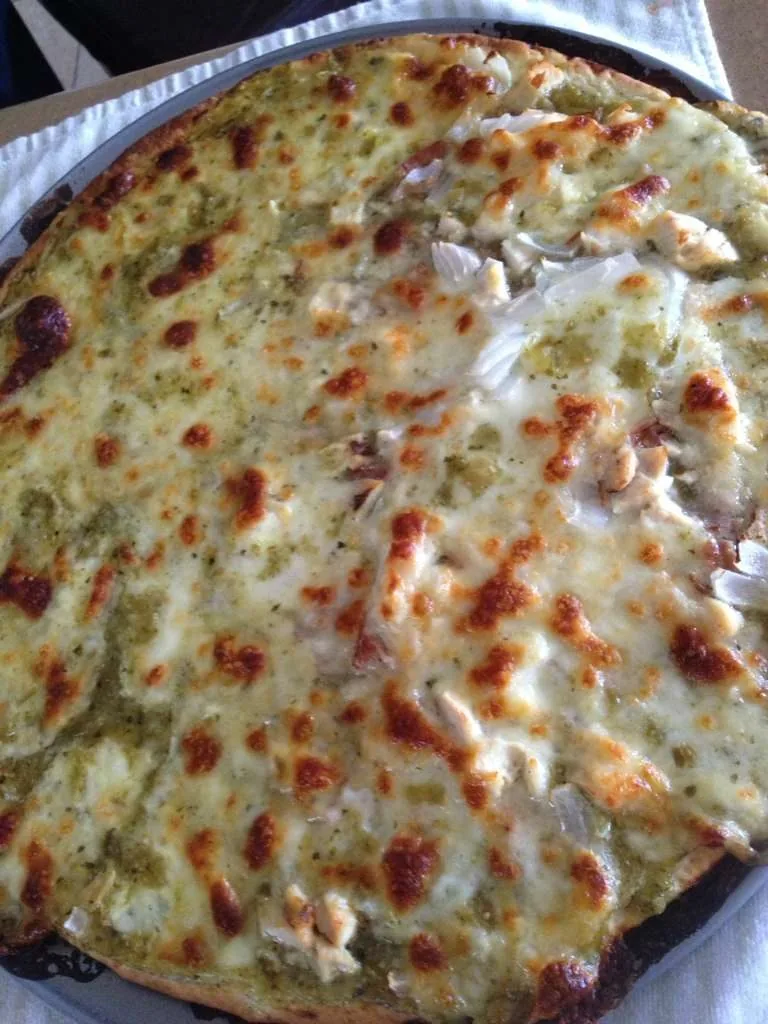 A pizza built on a salsa verde base, with melted cheese and chicken, on a dark tray.