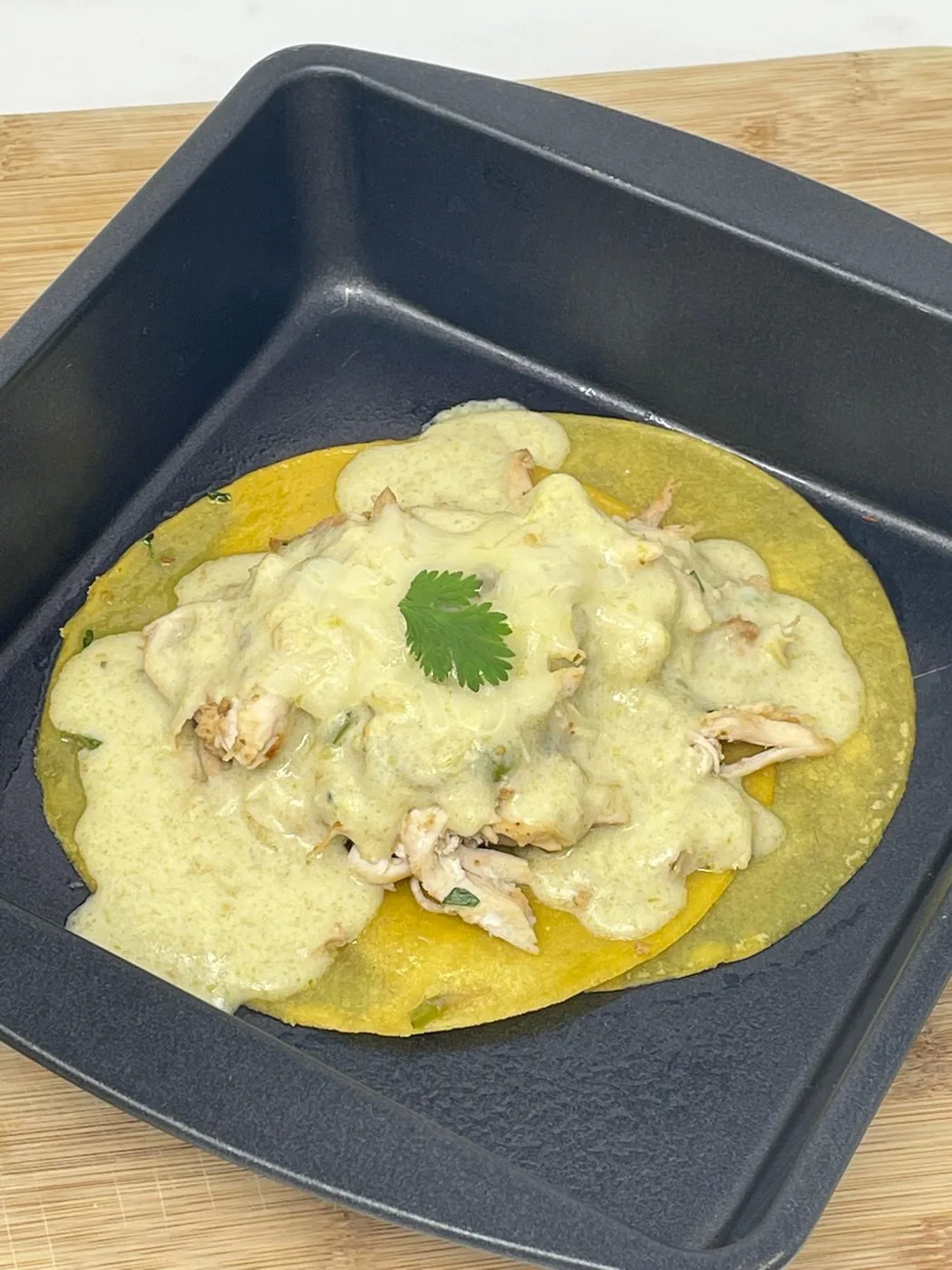 Tortilla with shredded chicken in salsa verde and cream, served in a dark square dish on a wooden board.