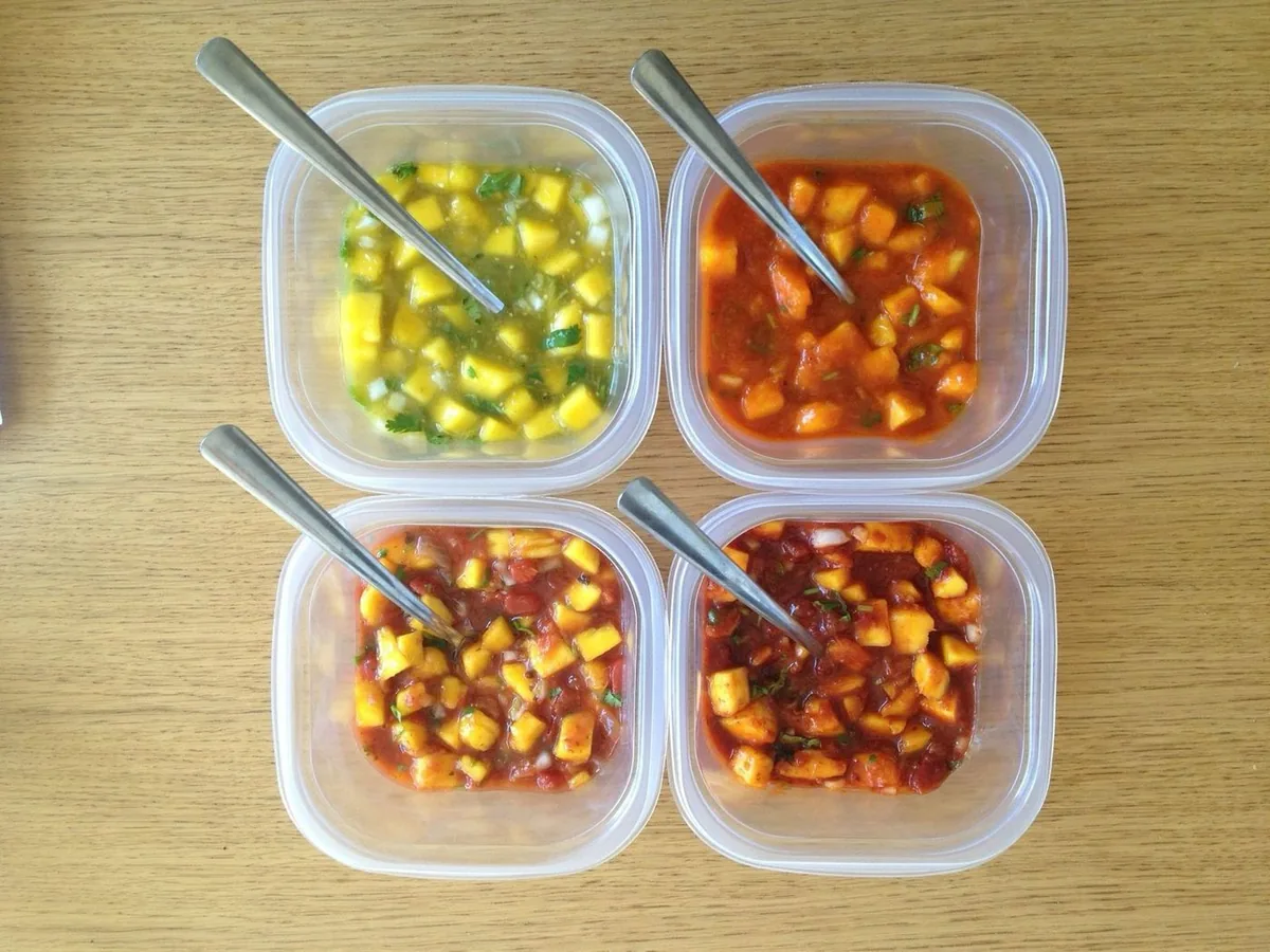 Four plastic tubs of mango salsa, each one sitting on a different-colored salsa base, seen from above.